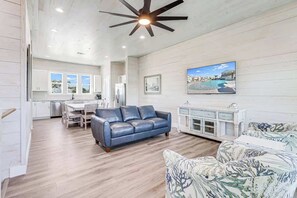 A spacious living area with a blue leather sofa, a patterned armchair, a dining table, and a kitchen in the background. - 151 Seven Palms, Ahoy Matey (Fulton)