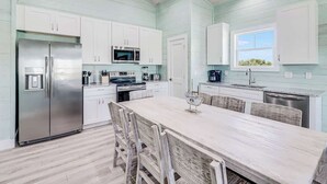 A kitchen with white cabinets, a stainless steel refrigerator, a microwave, and a dining area with a table and chairs. - 131 Seven Palms, Casa Grande (Fulton)