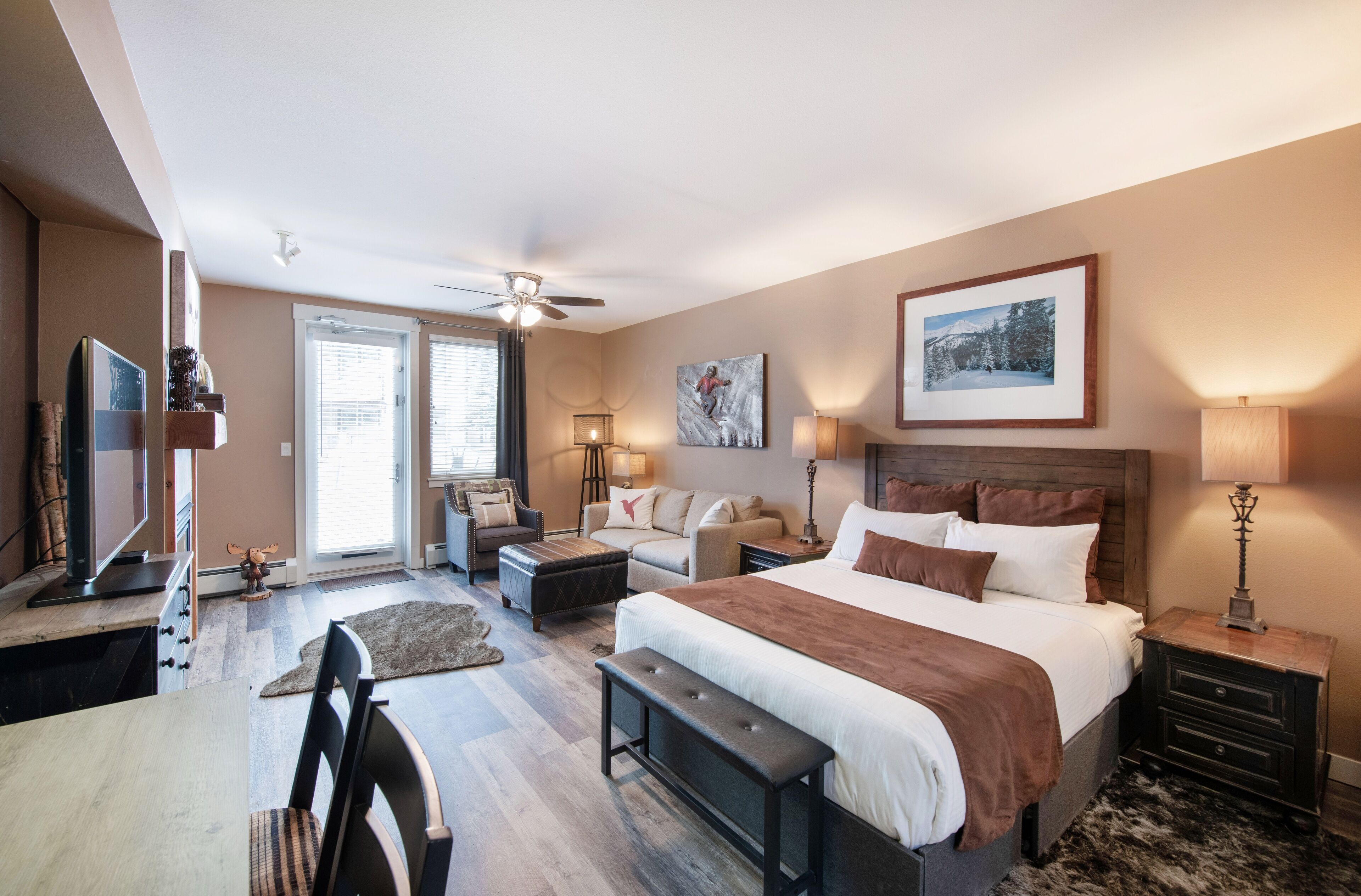 Une chambre spacieuse avec un grand lit, un bureau et une chaise, un ventilateur de plafond et une vue sur l’extérieur.