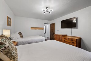 Un dormitorio con dos camas individuales, un aparador de madera, un televisor de pantalla plana y una lámpara en el techo.
