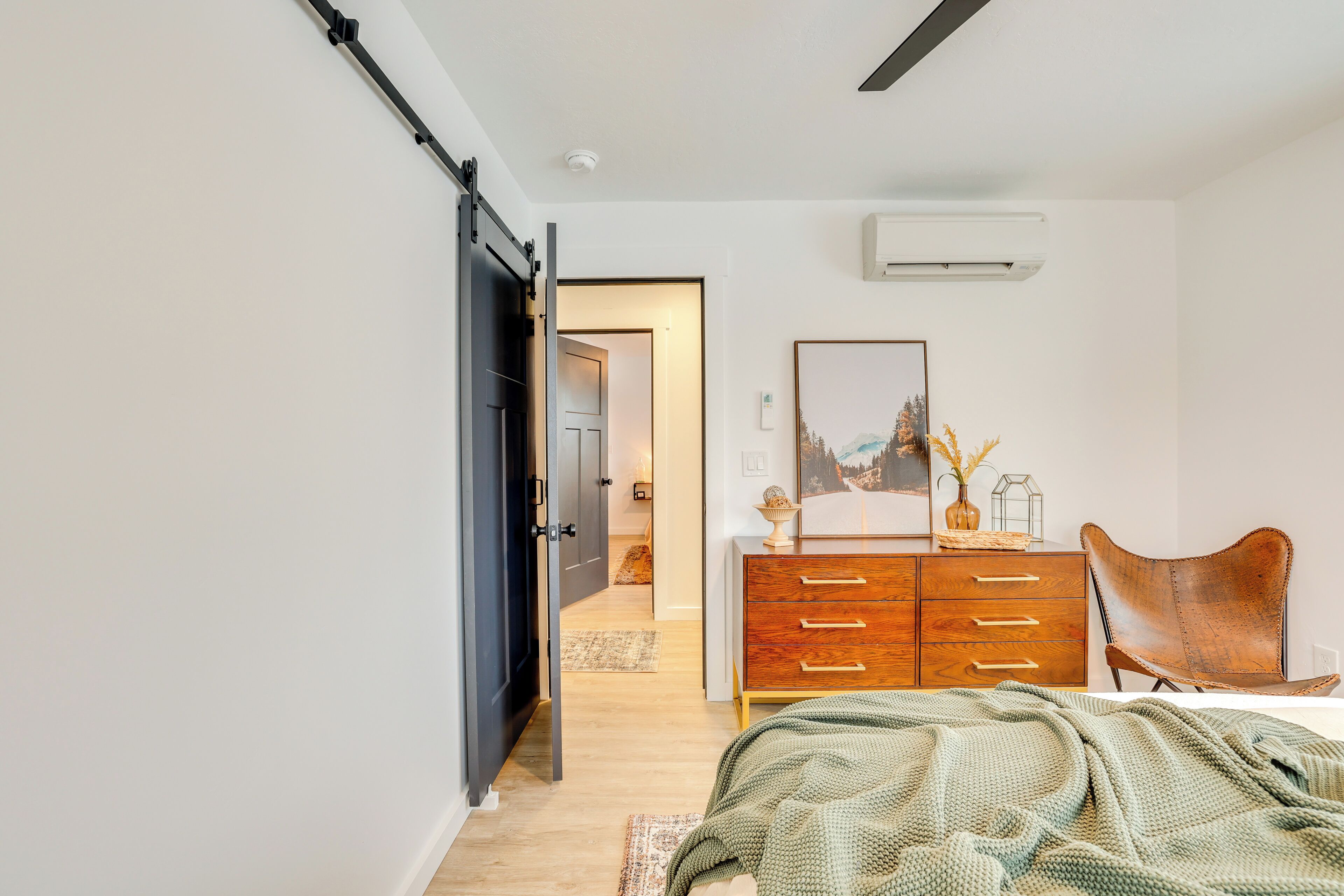 Ein Schlafzimmer mit Bett, Schminktisch, Stuhl und einer Tür zu einem weiteren Raum.