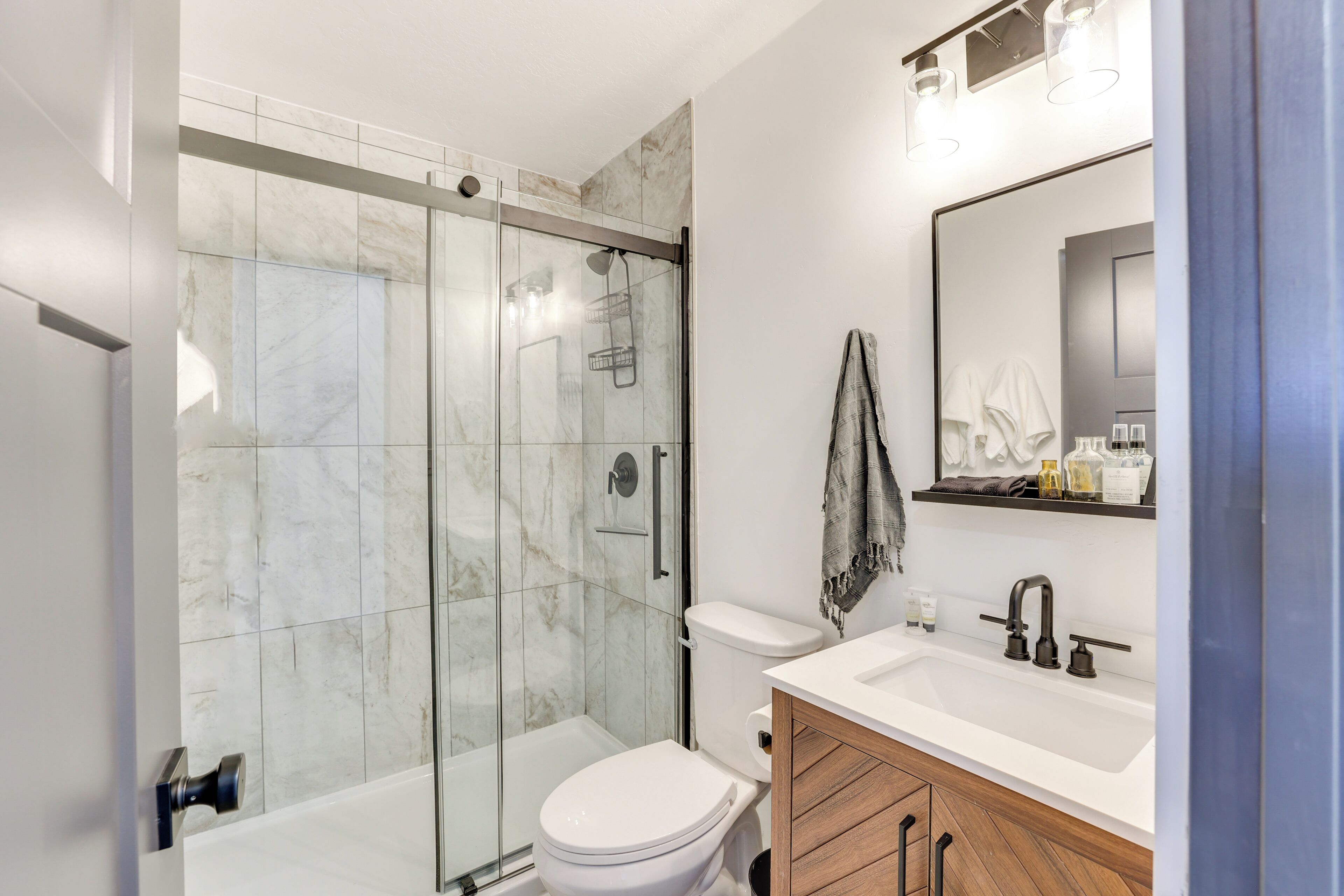 A modern bathroom with a glass-enclosed shower, a white toilet, and a wooden vanity with a sink.