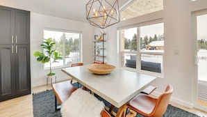 A modern dining area with a large table, chairs, a geometric pendant light, and a view of the outdoors. - Family-friendly Donnelly Home w/ Private Hot Tub! (Donnelly)