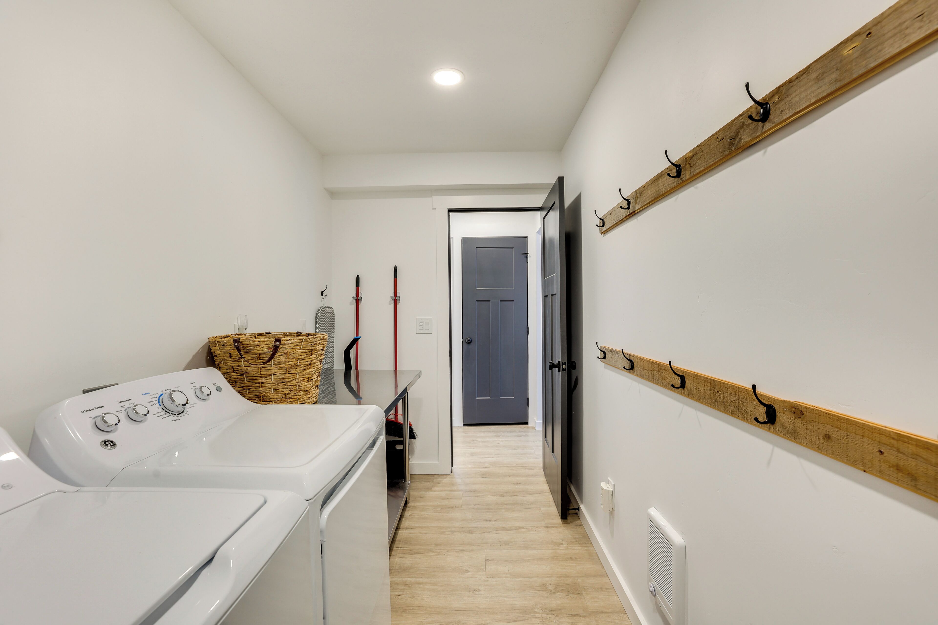 A laundry area with a washing machine, dryer, and a wooden shelf with hooks.