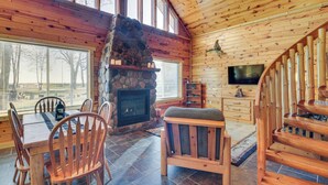 A cozy cabin interior with a stone fireplace, wooden furniture, and a TV mounted on the wall. - Eagle's Nest Cabin on Mille Lacs Lake: Boat + Fish (Garrison)