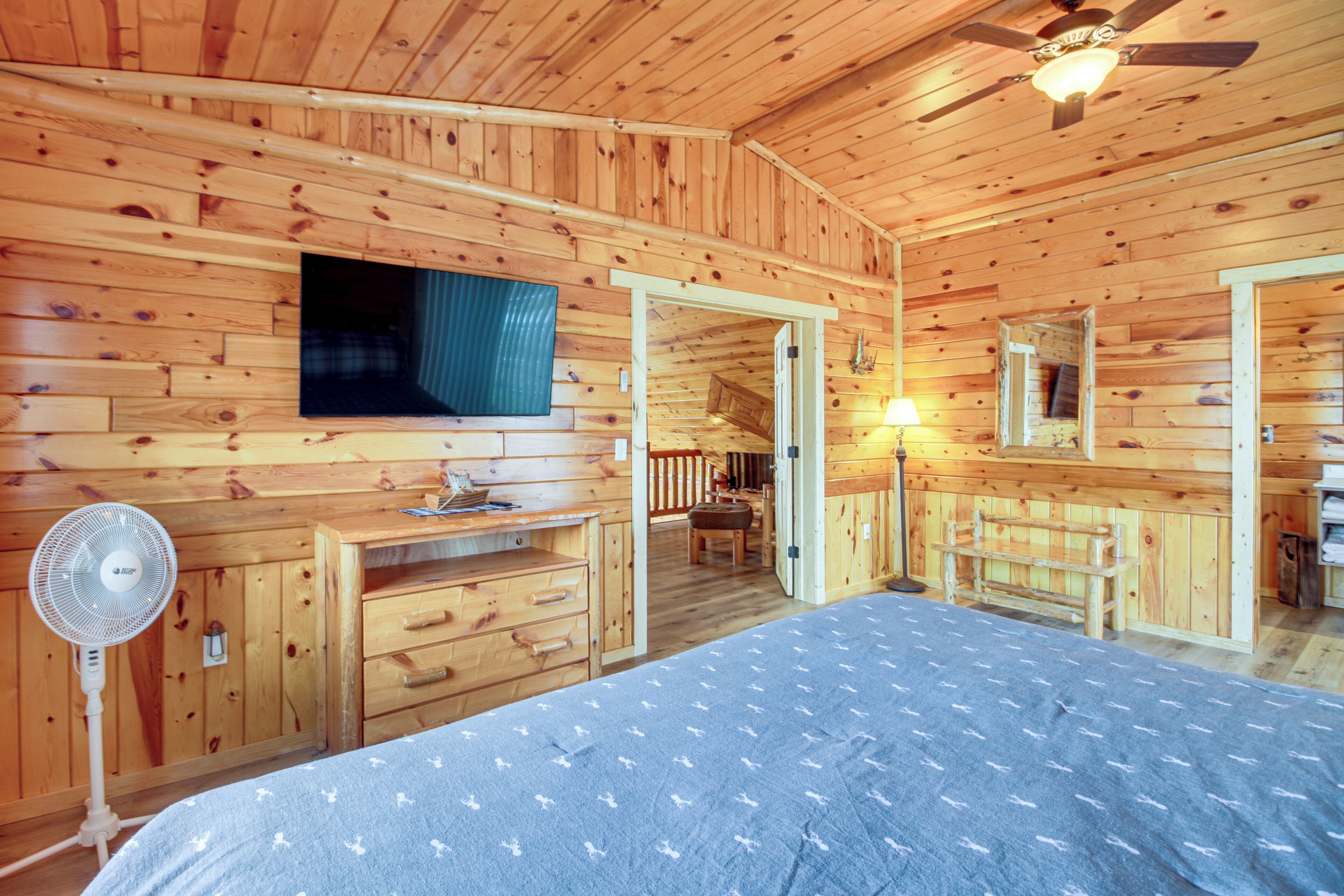 A wooden cabin bedroom with a bed, dresser, fan, and a ceiling fan.