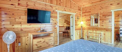 A wooden cabin bedroom with a bed, dresser, fan, and a ceiling fan.