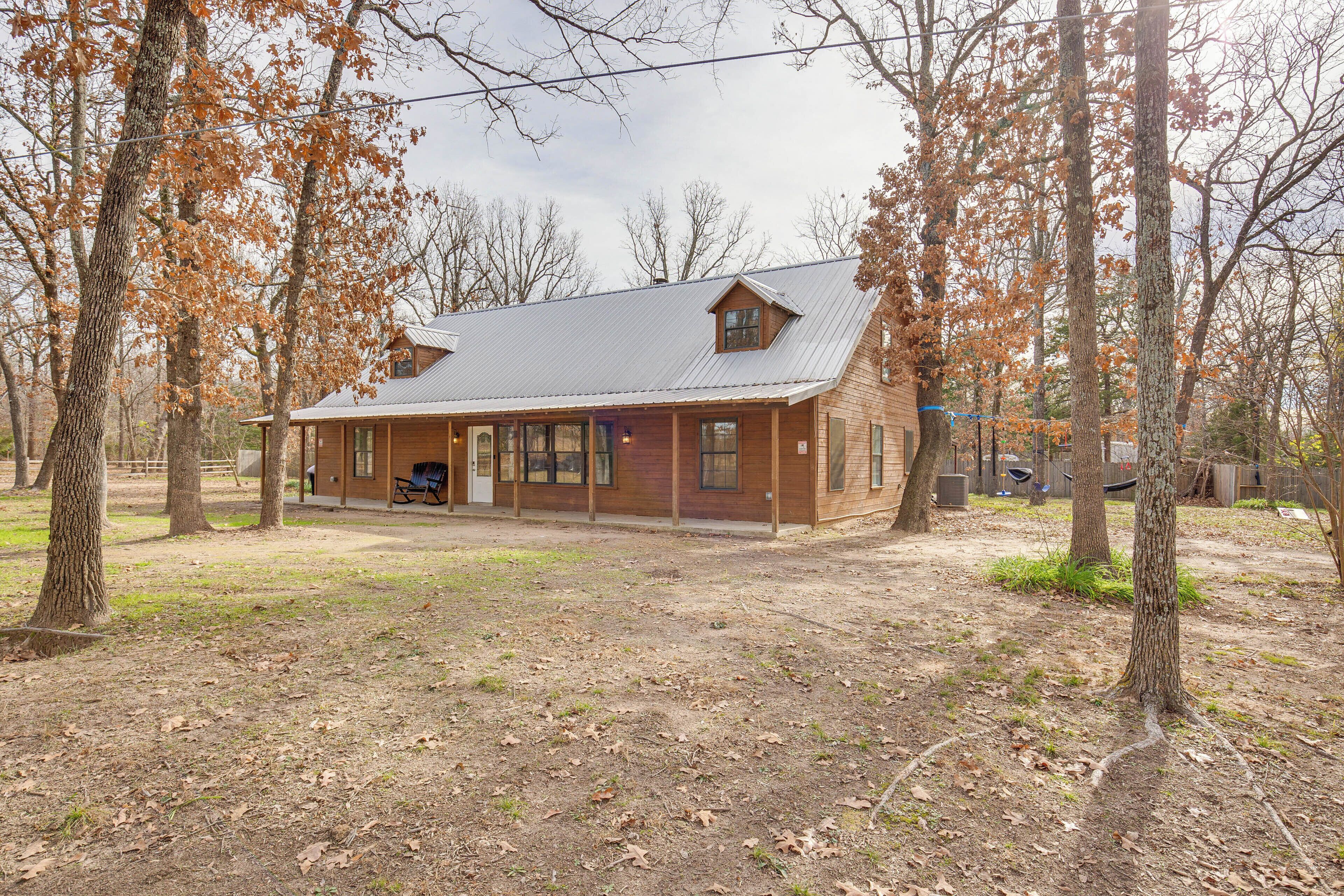 A rustic log cabin with a porch, surrounded by trees and a dirt yard.