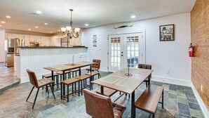 A spacious dining area with multiple tables and chairs, a kitchen in the background, and a wooden wall. - Near Lake Fork: Home w/ Fire Pit in Yantis! (Yantis)