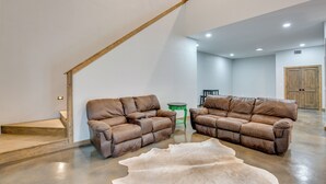 A spacious living area with two leather sofas, a wooden staircase, and a large fur rug. - Peaceful Yantis Retreat - 1 Mi to Lake Fork! (Yantis)