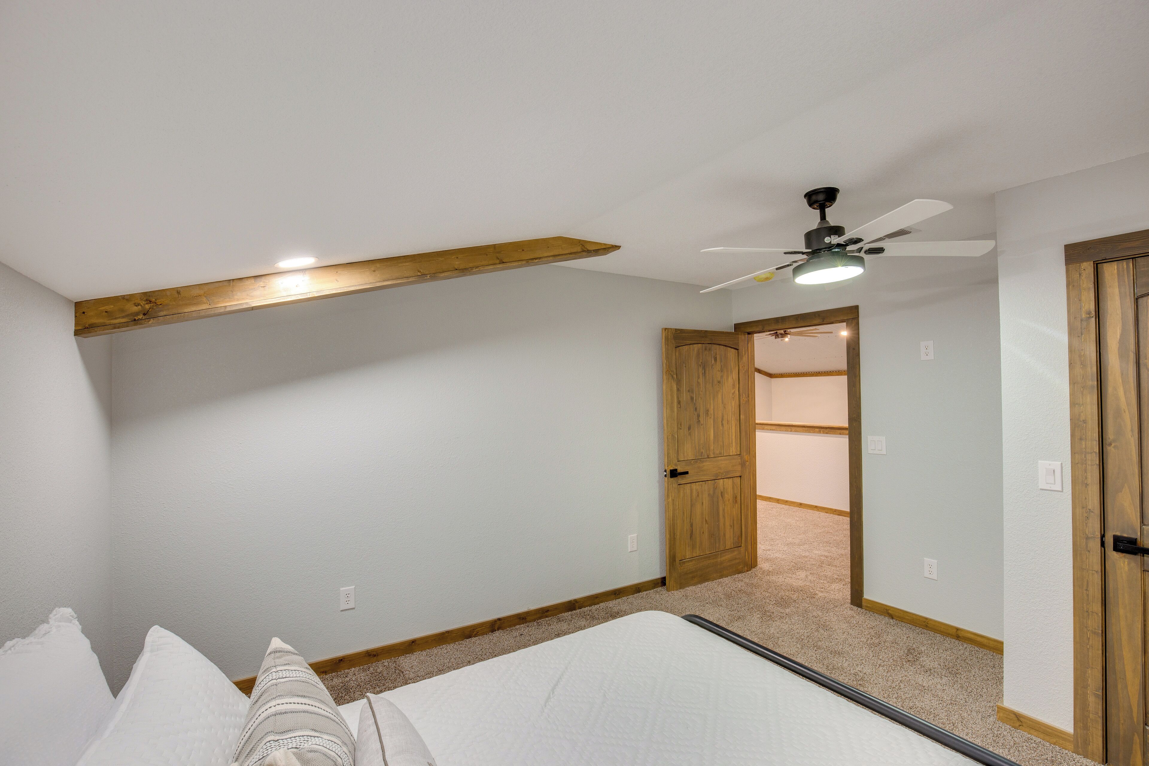 Une chambre à coucher avec un lit, des poutres en bois, un ventilateur de plafond et une porte donnant sur une autre pièce.