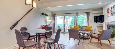 A modern living room with a glass dining table, comfortable seating, a fireplace, and a balcony with a view.