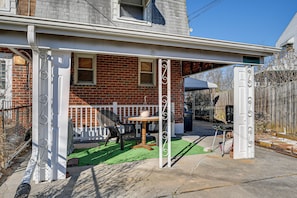 A covered patio with a table and chairs, a white fence, and a brick house in the background. - Maryland Abode w/ Patio: Near Baltimore Harbor (Baltimore)