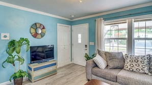A living room with a television, a sofa, and a potted plant. - Gulfport Vacation Rental w/ Patio & Game Room! (Gulfport)