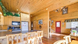 A wooden cabin interior with a kitchen area, wooden bar stools, and a dining table. - Pet-friendly Idaho Home on the Salmon River! (Salmon)