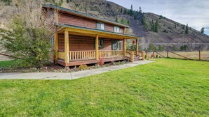 A log cabin with a porch, surrounded by a grassy yard and a hillside. - Pet-friendly Idaho Home on the Salmon River! (Salmon)