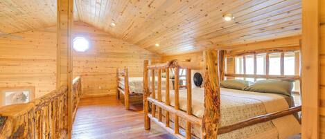A wooden cabin interior with a loft bed, a wooden staircase, and a large window.