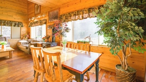 A wooden cabin interior with a dining table, chairs, a sofa, and a large window with curtains. - Pet-friendly Idaho Home on the Salmon River! (Salmon)