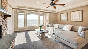 A living room with a stone fireplace, a ceiling fan, a large window with a mountain view, and a gray sofa. - Expansive Mountain Gem: Game Room, 3 Mi to Acton (Acton)