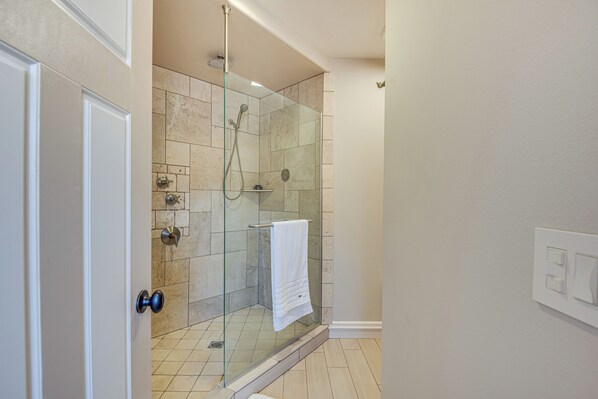 Un baño moderno con ducha de vidrio, azulejos color beige y una toalla blanca colgada en la pared.
