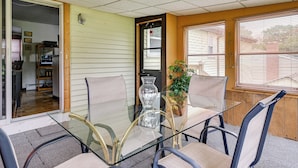 A glass-top table with four chairs, a vase, and a potted plant in a room with wooden walls and a door leading to another room. - Vintage Windsor Home: Private Yard & Covered Deck (Windsor)