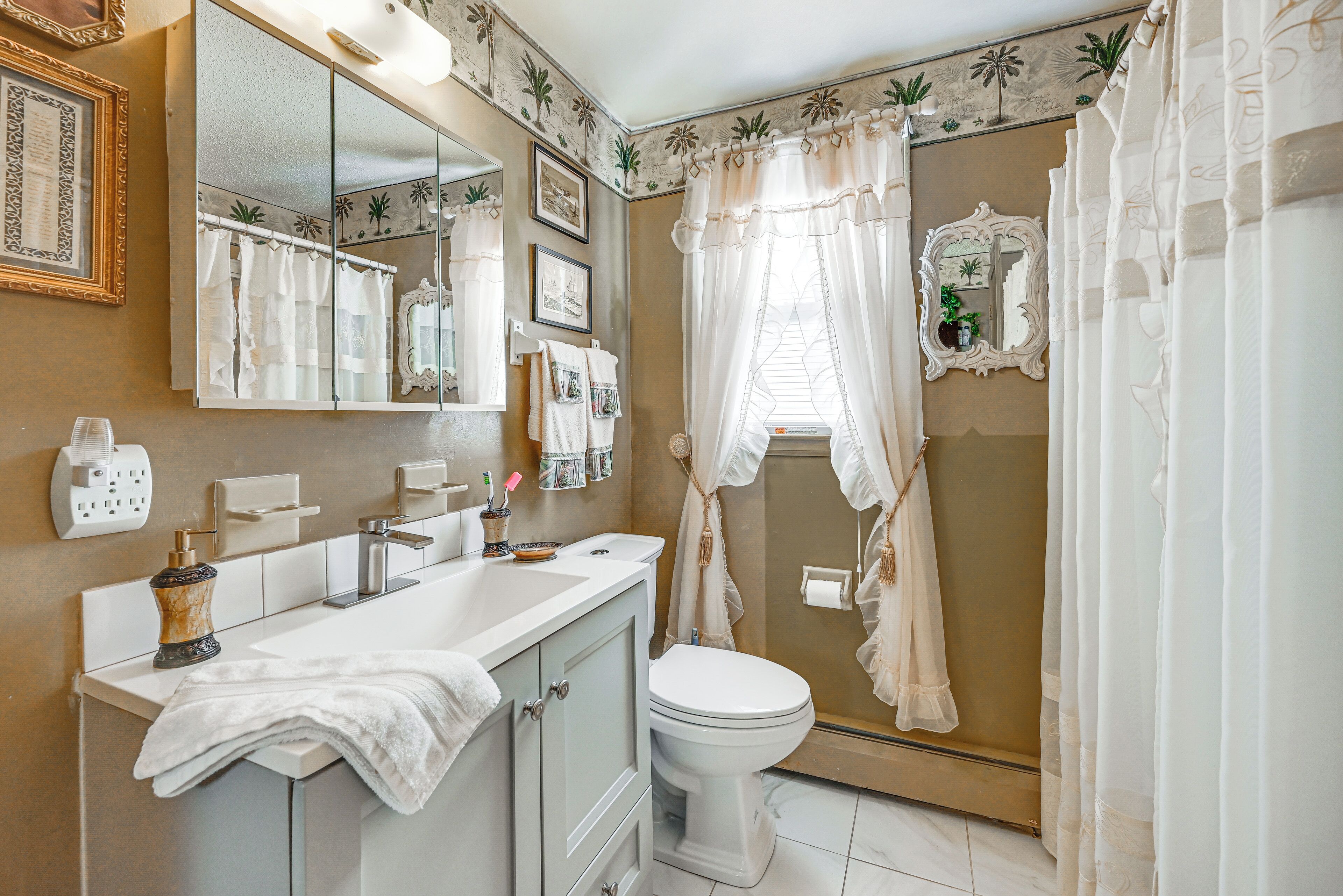 A bathroom with a vanity, sink, mirror, toilet, and shower curtain.