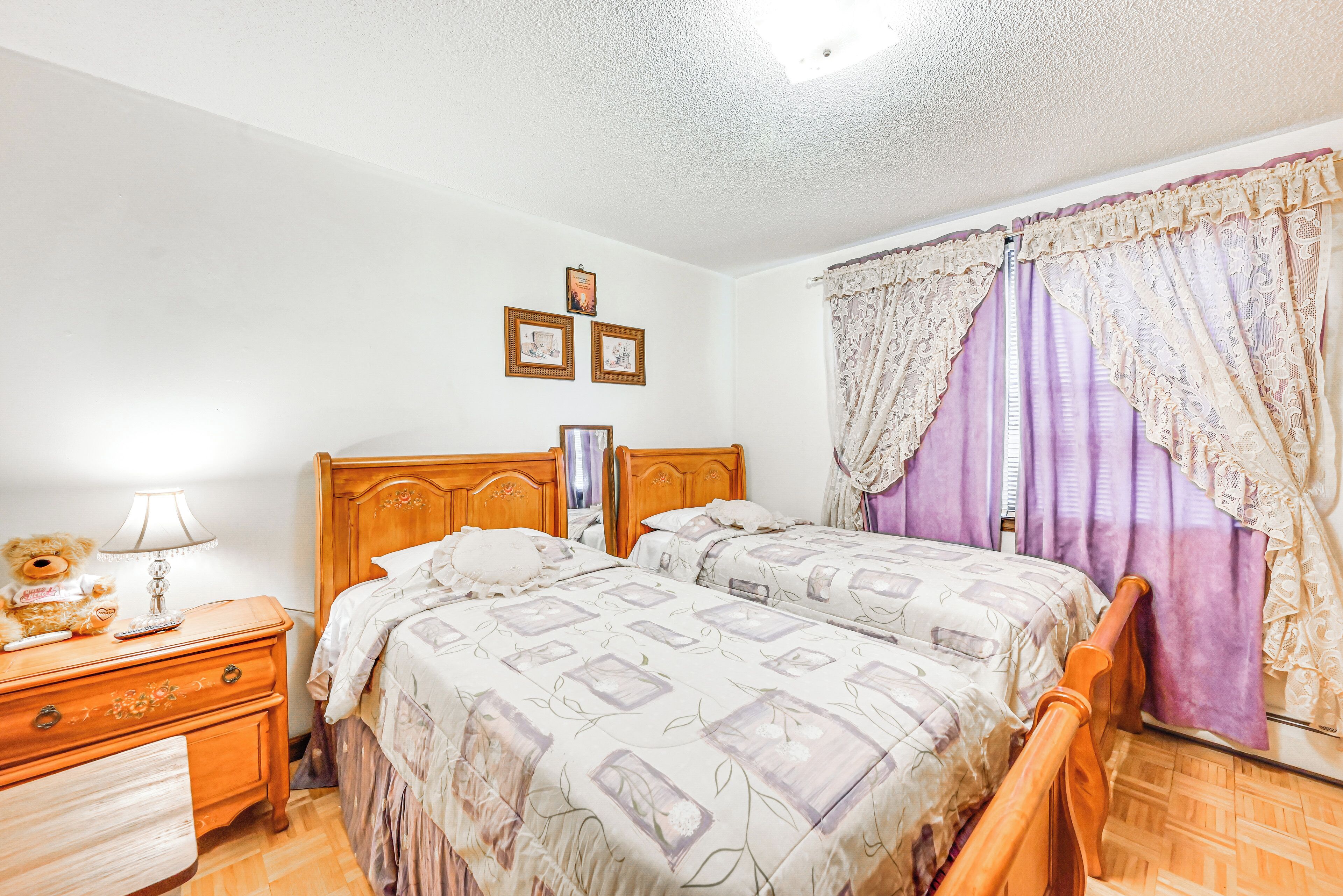 A bedroom with two beds, wooden headboards, a nightstand with a lamp, and a dresser.