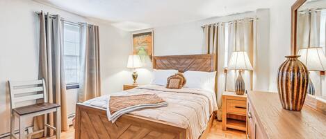 Ein Schlafzimmer mit einem hölzernen Bett, einem Nachttisch, einer Lampe, einem Stuhl und einem großen Spiegel.