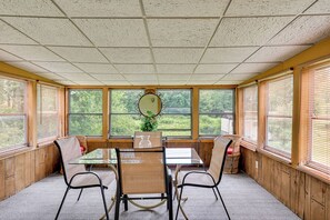 A sunroom with a glass table, four chairs, a mirror, and a potted plant. - Vintage Windsor Home: Private Yard & Covered Deck (Windsor)