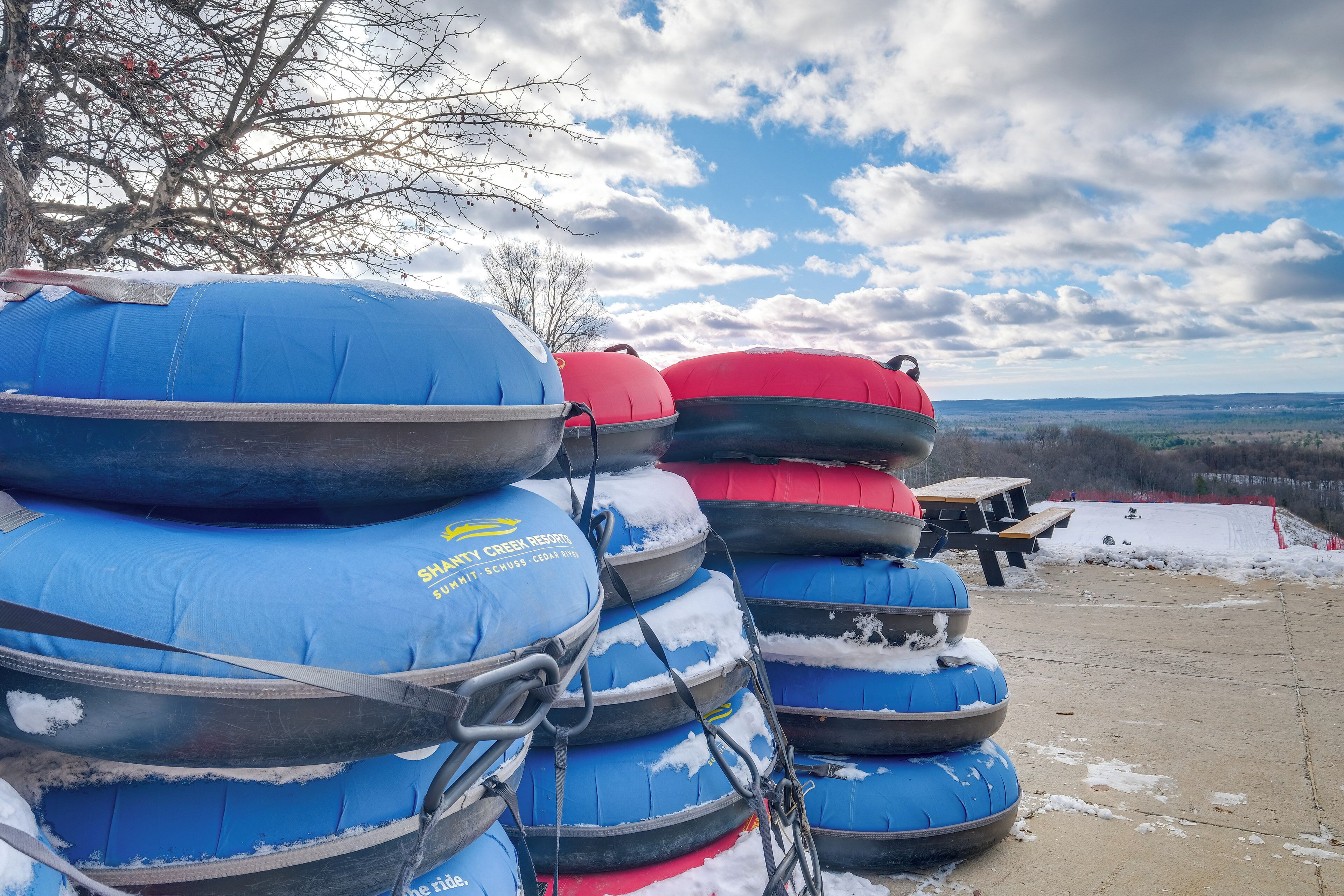 A stack of blue and red inflatable rafts with snow on the ground and a picnic table in the background.