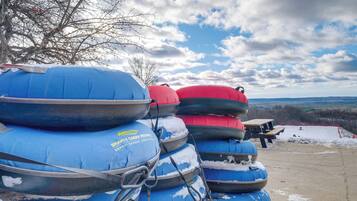 A stack of blue and red inflatable rafts with snow on the ground and a picnic table in the background.