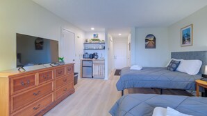 A hotel room with two beds, a TV, a wooden dresser, a kitchenette, and a hallway leading to another room. - Bellaire Condo - Walk to Shanty Creek Resort! (Bellaire)