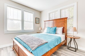 A bedroom with a wooden bed, a blue quilt, and a small round table with a lamp.
