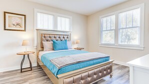 A bedroom with a large bed, two bedside tables, a headboard, and two windows with blinds. - Quiet Grove Hill Cottage w/ Wraparound Deck! (Grove Hill)