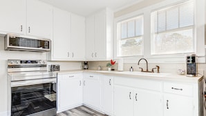 A modern kitchen with white cabinets, stainless steel appliances, and a window with blinds. - Quiet Grove Hill Cottage w/ Wraparound Deck! (Grove Hill)