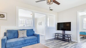 A living room with a blue sofa, a wooden coffee table, and a flat-screen TV on a stand. - Quiet Grove Hill Cottage w/ Wraparound Deck! (Grove Hill)
