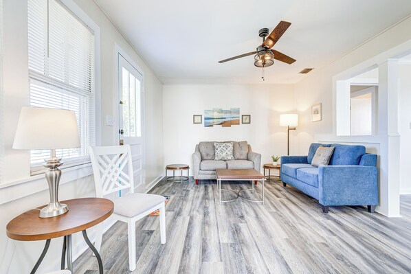 A living room with a sofa, coffee table, and chairs, a ceiling fan, and a lamp.