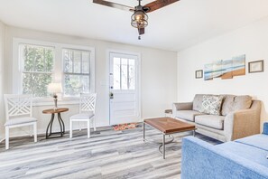 A living room with a sofa, chairs, a coffee table, a ceiling fan, and artwork on the wall.
