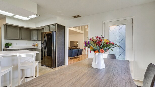 A modern kitchen with white cabinets, a wooden dining table, and a vase of flowers. - Tranquil Fort Wayne Home: 7 Mi to Downtown (Fort Wayne)