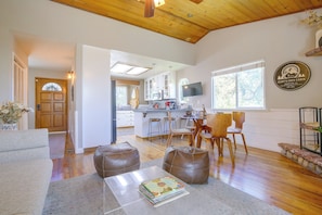 A modern interior with a wooden ceiling, a kitchen with white cabinets, a dining area with wooden chairs, and a living room with a sofa and ottomans. - Lake, Trails & Slopes! Family Cottage in Crestline (Crestline)