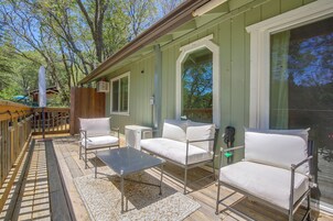 Un área de estar al aire libre techada, con sillas blancas acolchadas y una mesa, rodeada por una terraza de madera y una cerca verde.