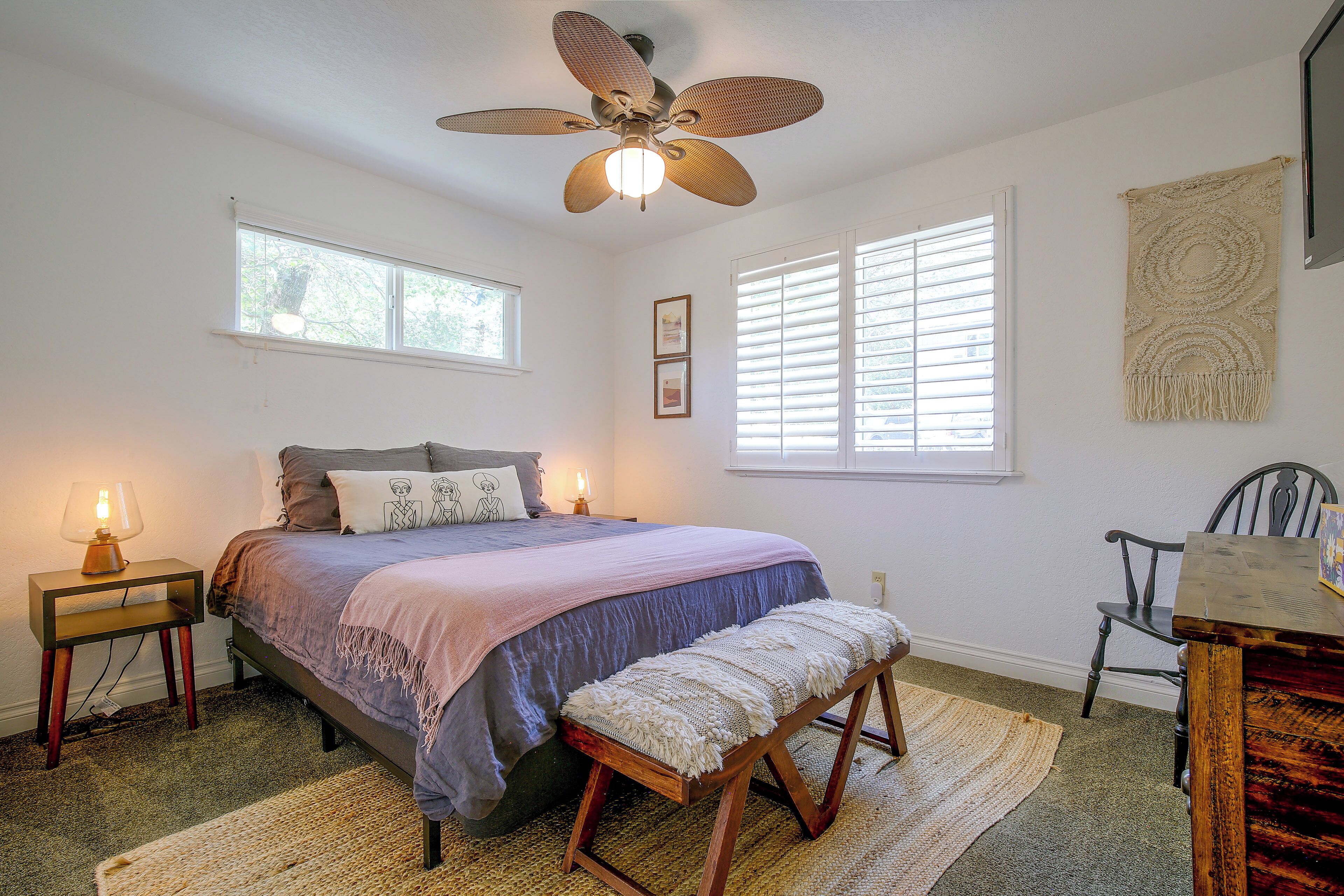 Une chambre à coucher comprenant un lit, des lampes de chevet, un ventilateur de plafond, une fenêtre et une tapisserie murale.