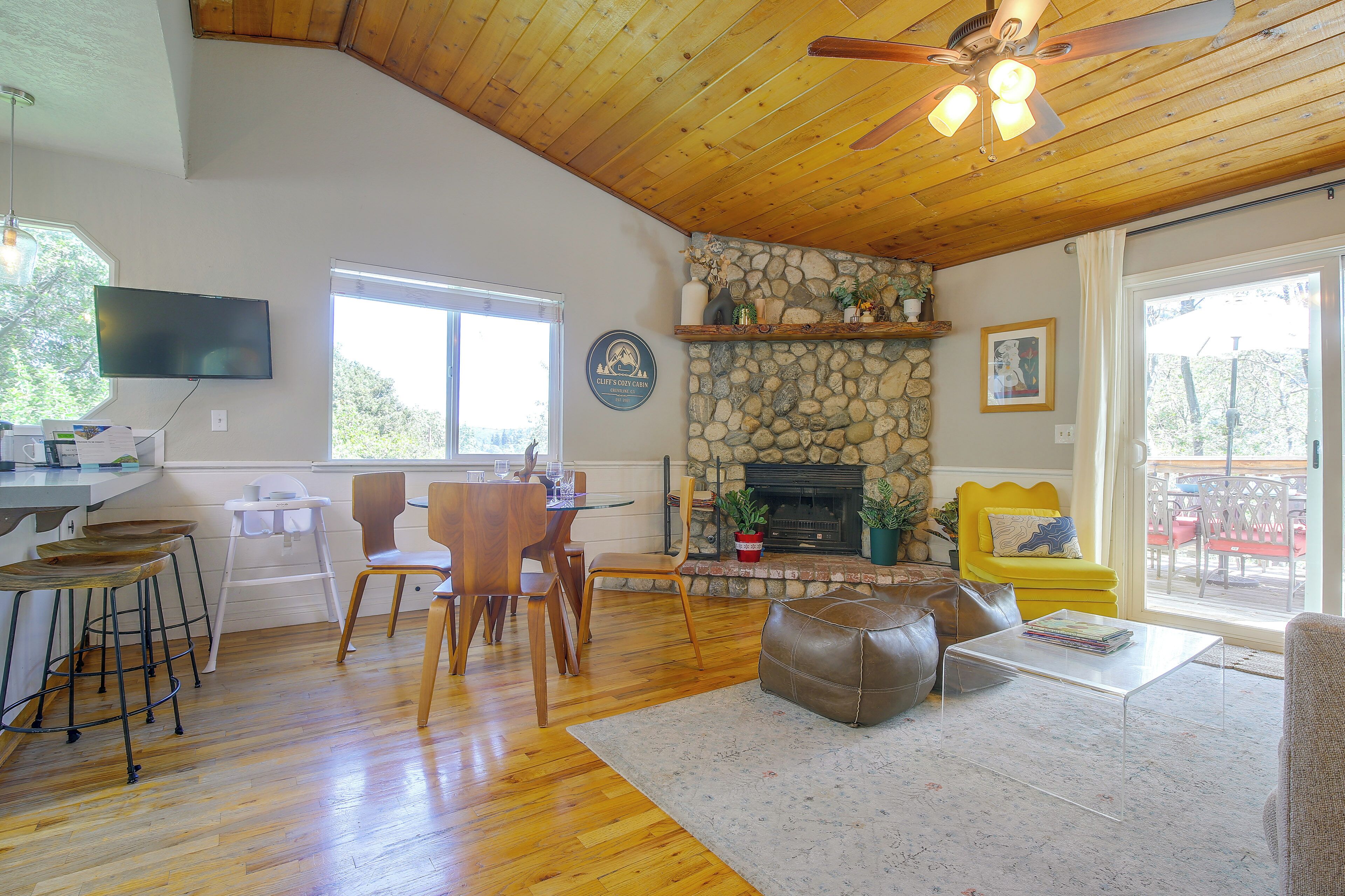 A spacious living area with a stone fireplace, wooden ceiling, and a dining table with chairs.