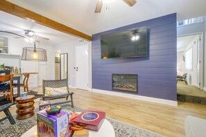 Una sala de estar con chimenea, un televisor montado en la pared y un comedor con sillas y una mesa.