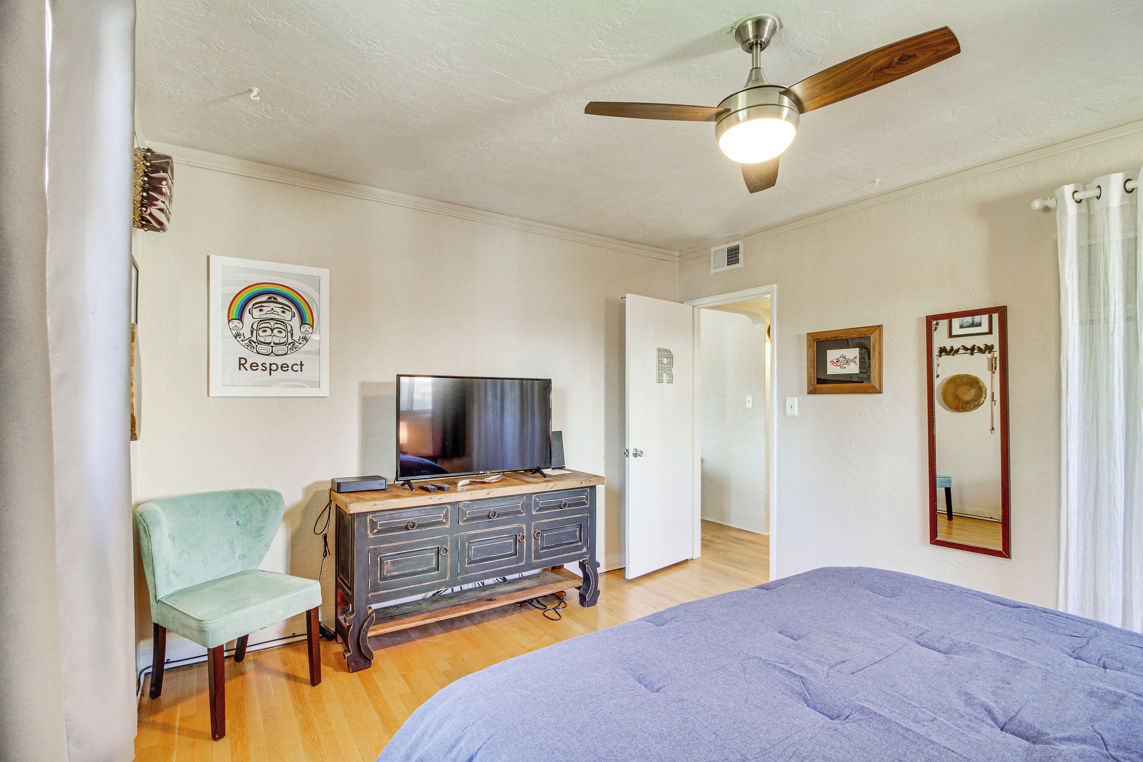 Une chambre à coucher avec un lit, un téléviseur posé sur une commode, une chaise et un ventilateur de plafond.