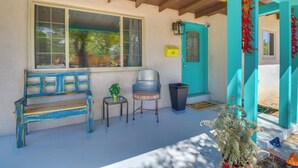 A porch with a blue bench, a small table with a plant, a trash can, and a teal door. - Dog-friendly Albuquerque Home: 1 Mi to U of NM! (Albuquerque)
