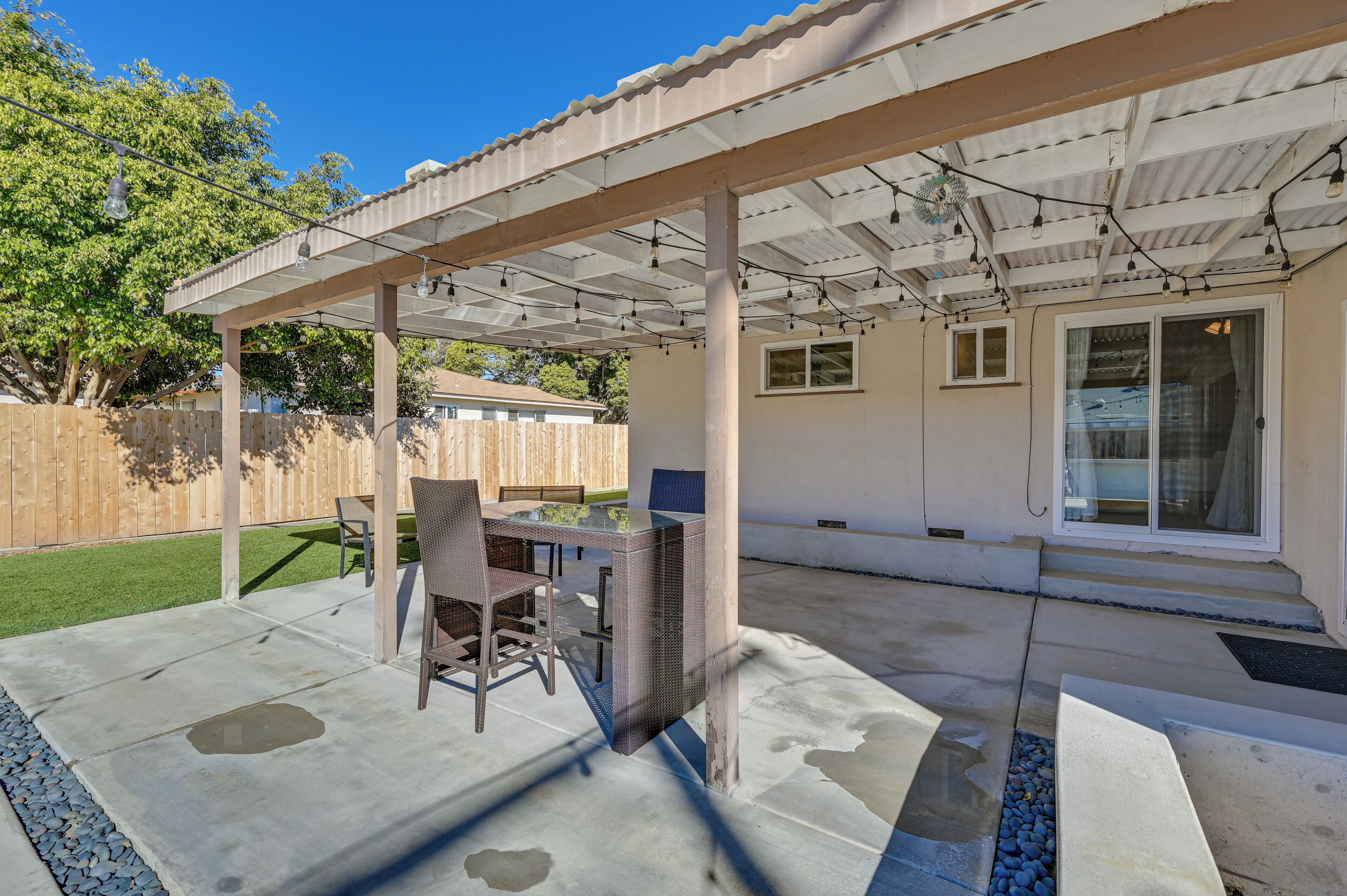 Une terrasse couverte avec une table et des chaises en verre, une clôture en bois et une maison en arrière-plan.