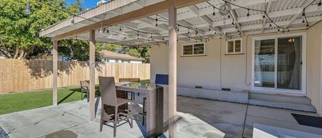 Une terrasse couverte avec une table et des chaises en verre, une clôture en bois et une maison en arrière-plan.