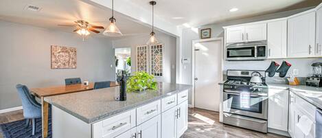 A modern kitchen with white cabinets, a granite countertop, stainless steel appliances, and pendant lighting.