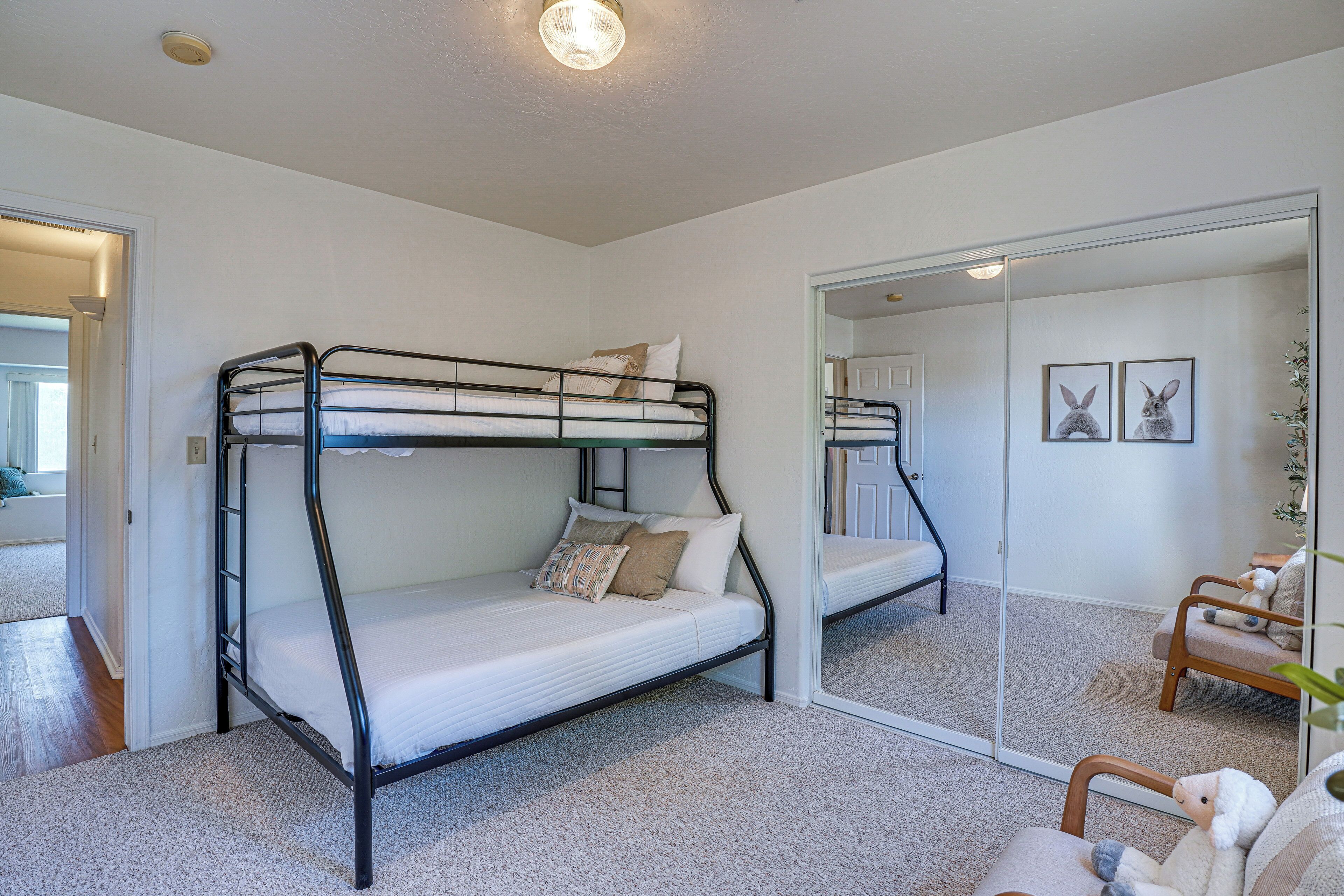 Une chambre avec un lit superposé, un miroir, une chaise et une porte donnant sur une autre pièce.